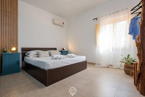 A modern bedroom with a wooden bed, a nightstand, a wall-mounted air conditioner, and a window with sheer curtains.