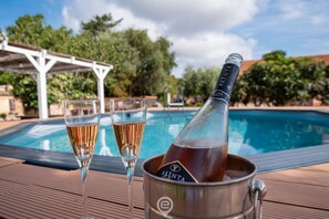 A poolside setting with two glasses of champagne and a bottle in a bucket.