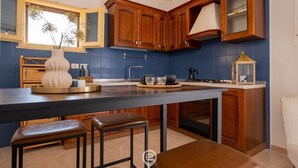 A modern kitchen with wooden cabinets, a central island with stools, and a window with natural light.