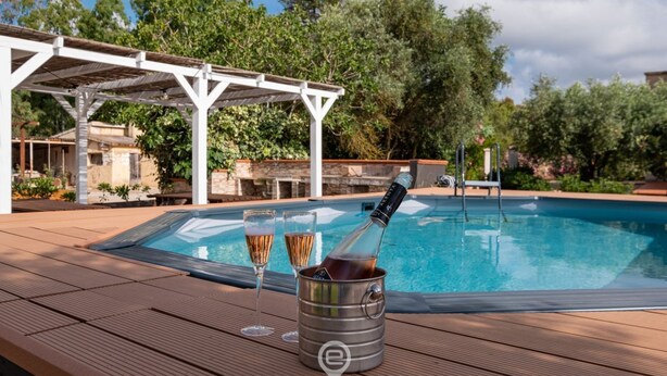 A poolside area with a pergola, a hot tub, and two glasses of champagne.