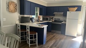 A modern kitchen with dark blue cabinets, a white refrigerator, and a wooden island with bar stools. - Charming pet-friendly, beach home near Bethany Beach- great local attractions.  (Ocean View)