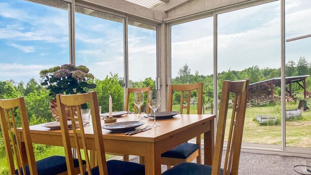 Ein Essbereich mit großem Tisch und Stühlen, großen Fenstern und Blick ins Freie.