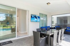 A modern outdoor dining area with wicker furniture and a glass table, overlooking a pool. - 5BR Themed Home with Pool Near Disney (Davenport)