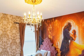 A room with a chandelier, patterned wallpaper, a large mural, and a bed with a decorative headboard.
