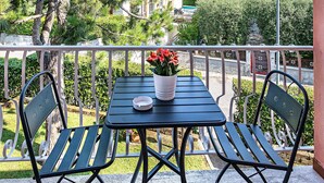 A balcony with a table and chairs, a potted plant, and a view of trees and buildings. - Il Quadrifoglio D4 Apartment by Wonderful Italy (Sirmione)