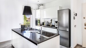 A modern kitchen with white cabinetry, a stainless steel refrigerator, and a black pendant light. - Il Quadrifoglio D4 Apartment by Wonderful Italy (Sirmione)