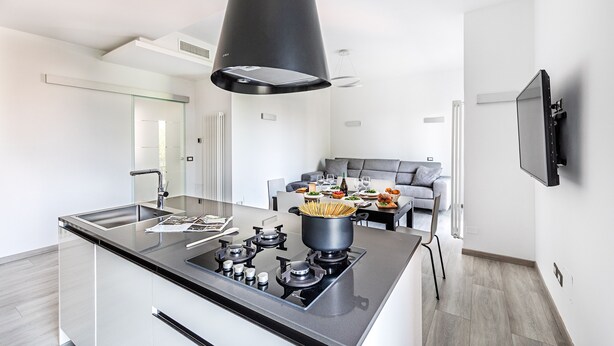 A modern kitchen with a central island, a dining area with a grey sofa, and a TV mounted on the wall. - Il Quadrifoglio D4 Apartment by Wonderful Italy (Sirmione)