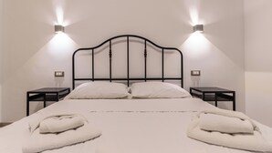 A neatly made bed with two pillows, a headboard with vertical lines, and two bedside tables with wall-mounted lights. - Il Quadrifoglio D4 Apartment by Wonderful Italy (Sirmione)