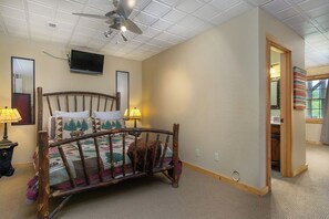Ein Schlafzimmer mit einem hölzernen Bett, einem Deckenventilator, einem an der Wand montierten Fernseher und einer Tür zu einem weiteren Raum.