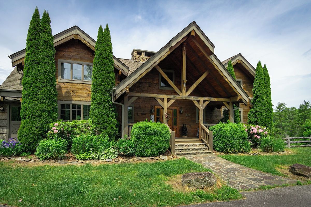 A log cabin with a stone pathway leading to the entrance, surrounded by lush greenery and tall trees.
