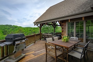 A wooden deck with a grill, outdoor seating, and a view of a forested area. - Mtn Views, Sunsets, WiFi, Fireplace, River & More! (Burnsville)