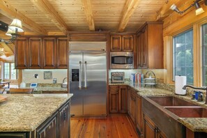Une cuisine dotée de meubles en bois, d’appareils électroménagers en acier inoxydable, de plans de travail en granit et d’une grande fenêtre.