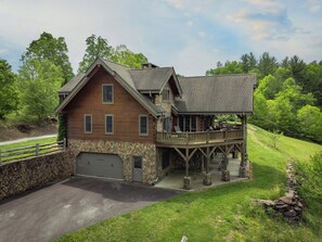 Eine zweistöckige Holzhütte mit Steinuntergrund, einer Garage und einer Veranda mit Sitzgelegenheiten.