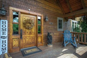 Eine Holzhütte mit einer Haustür, einem Willkommenskranz, einer Bärenstatue und einem blauen Adirondack-Sessel auf der Veranda.
