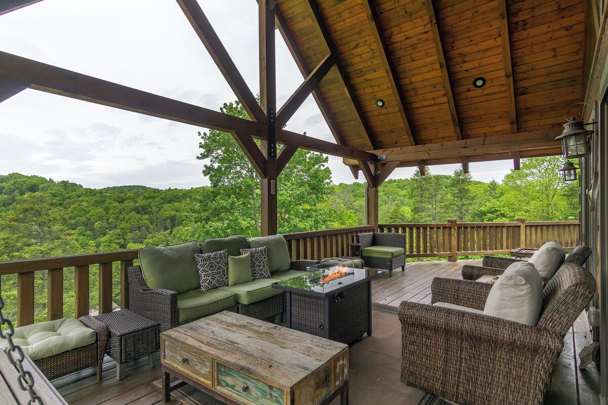 An outdoor deck with a wooden ceiling, wicker furniture, and a view of a forested area.
