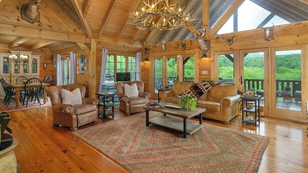 L’intérieur de cette vaste cabane en rondins est aménagé avec de nombreux coins salon, un lustre et de grandes fenêtres qui offrent une vue sur la forêt environnante.