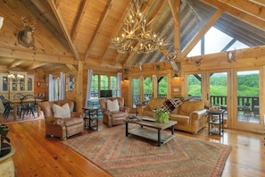 Un intérieur spacieux en bois, avec un plafond haut, un lustre et de grandes fenêtres offrant une vue sur l’extérieur.