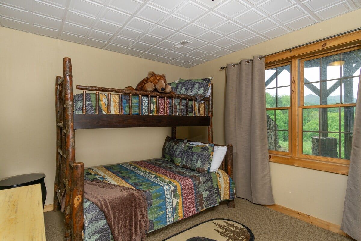 Dormitorio con literas, ventana, escalera de madera y colcha estampada.