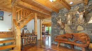 Un escalier en bois mène à une salle à manger dont un mur est en pierre et orné de têtes de cerf fixées au mur.