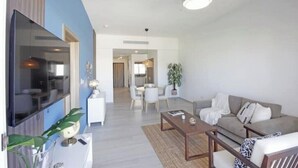 A modern living room with a flat-screen TV, a sofa, a coffee table, and a dining area with a table and chairs. - Exquisite 2-Bed/2-Bath Retreat by Hard Rock Hotel (Bavaro)