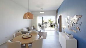 A modern living room with a round wooden table, white sofas, and a blue accent wall with a world map. - Exquisite 2-Bed/2-Bath Retreat by Hard Rock Hotel (Bavaro)