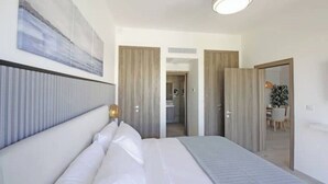 A modern hotel room with a large bed, a painting on the wall, and a view into the bathroom through a door. - Exquisite 2-Bed/2-Bath Retreat by Hard Rock Hotel (Bavaro)