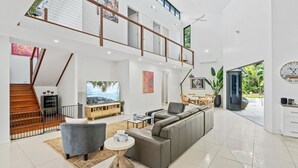 Un salón amplio con techo alto, un sofá grande, un televisor y una escalera que sube a un nivel superior.