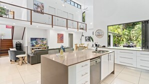 Una cocina moderna con una isla central, un comedor con una mesa alta y una sala de estar con sofá y televisor.