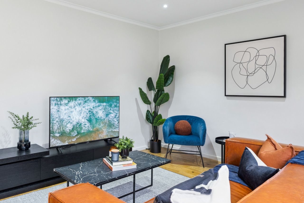 A modern living room with a flat-screen TV, a blue armchair, a sofa, and a coffee table.