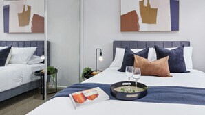 A modern hotel room with a large bed, two bedside tables, a nightstand, and a mirror.