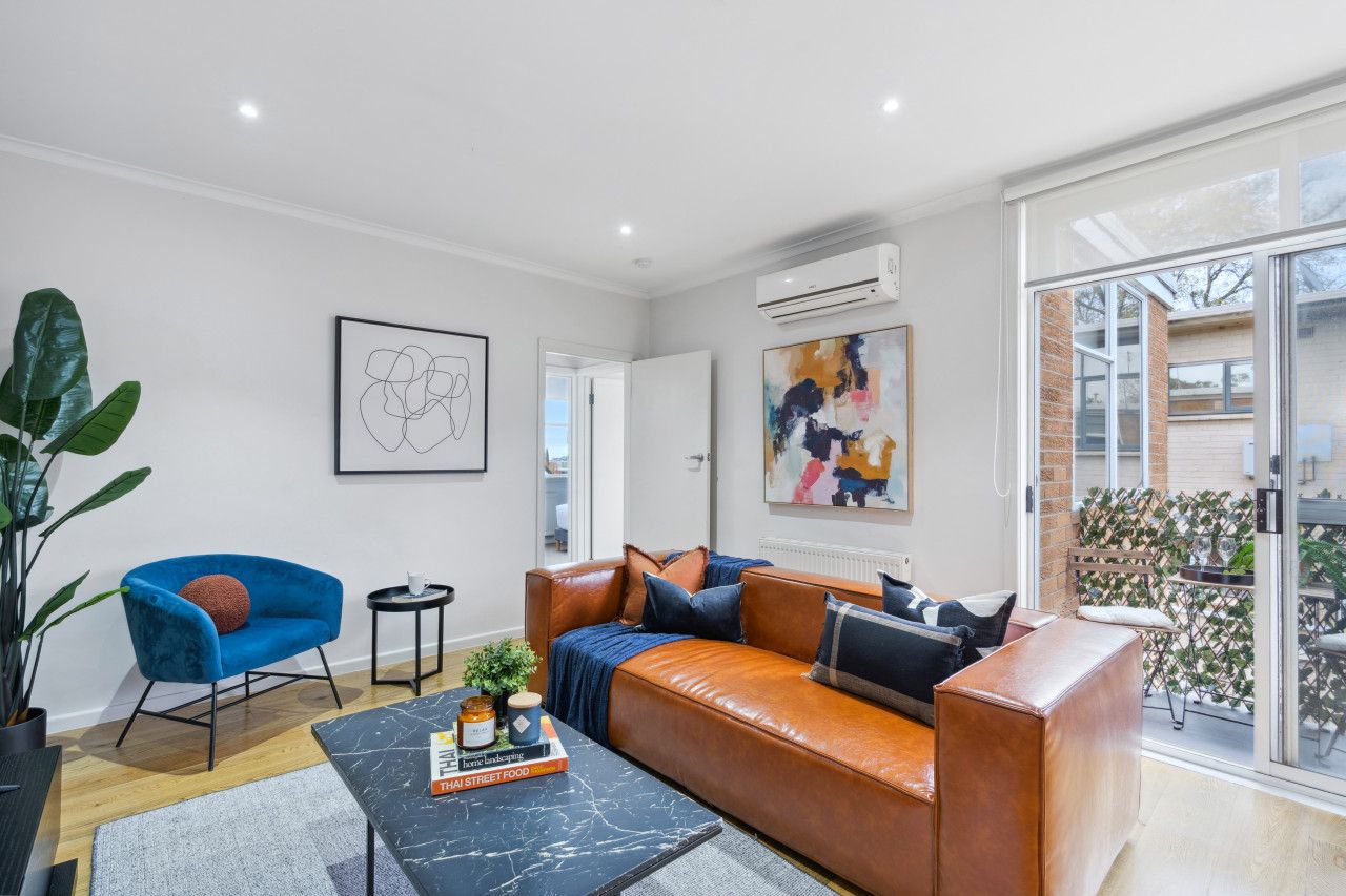 A modern living room with a leather sofa, a blue armchair, and a coffee table. There is a large window providing a view of the outside.