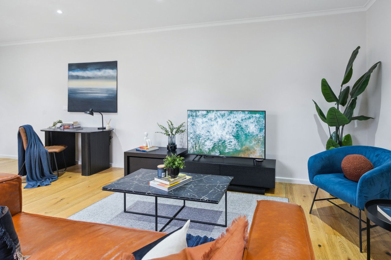 A modern living room with a flat-screen TV, a black coffee table, a blue armchair, and a large plant.