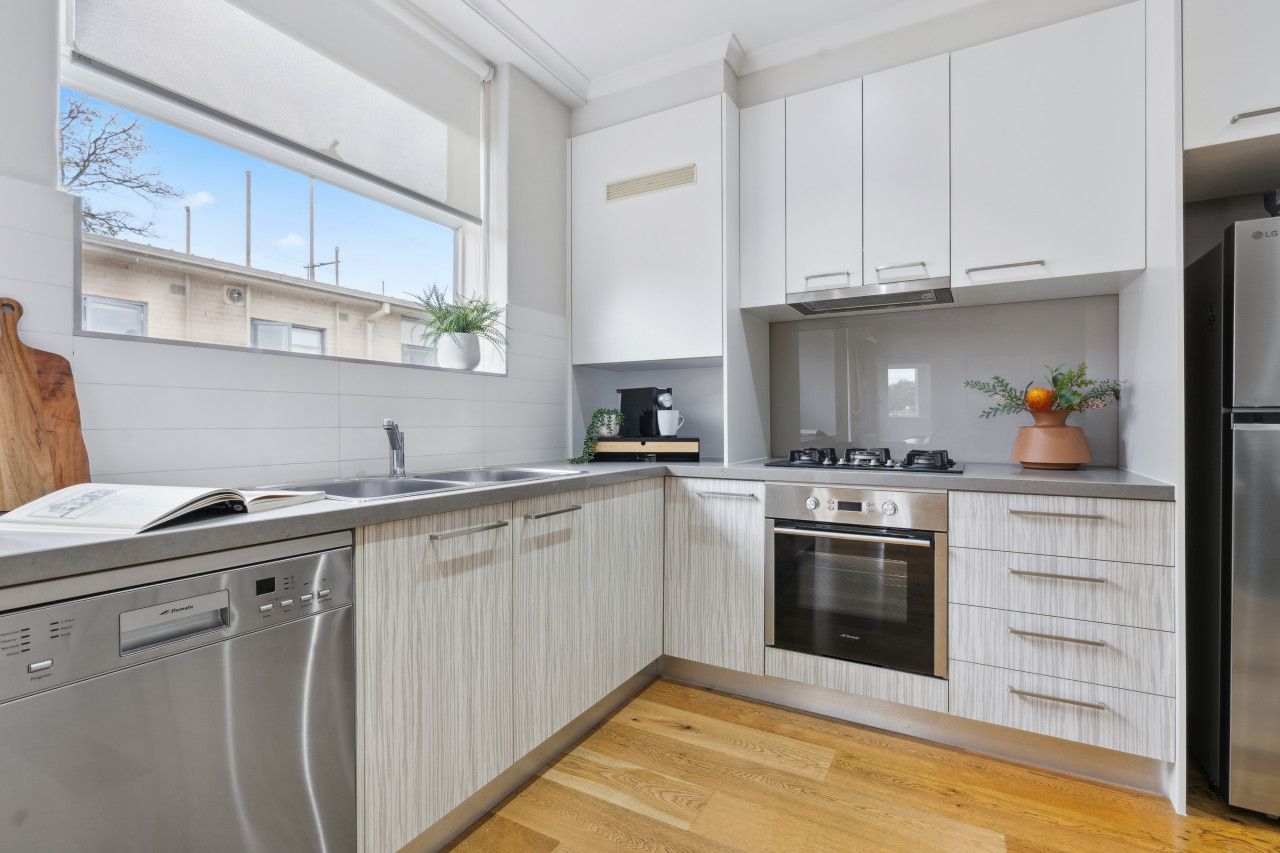 Una cocina moderna con armarios blancos, lavavajillas, horno y refrigerador.