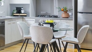 A modern kitchen with white cabinets, a stainless steel refrigerator, and a dining area with a glass table and chairs.
