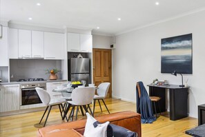 A modern kitchen with white cabinets, a stainless steel refrigerator, and a dining area with a table and chairs. - The Fulton Residence (Saint Kilda East)