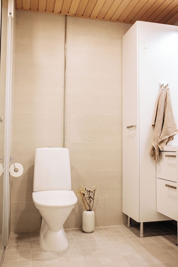A bathroom with a toilet, a cabinet, and a vase with dried flowers.