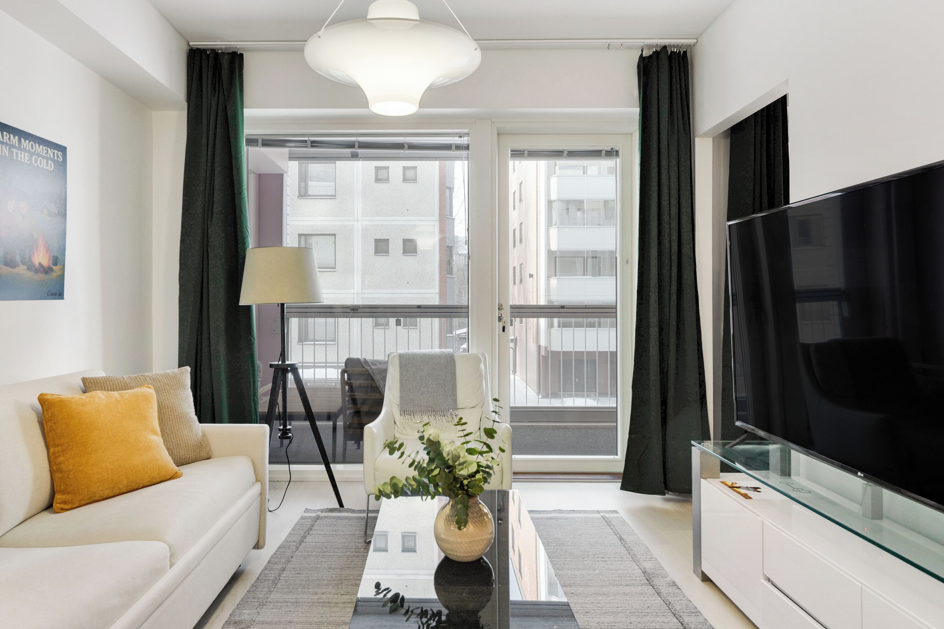 Un salon moderne avec un canapé, une table basse en verre, un téléviseur et une vue sur les immeubles par les fenêtres.