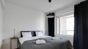 A modern bedroom with a large bed, a bedside table, a floor lamp, and a window with curtains. - Vapari - Tampere Soccer Stadium by Come in! (Tampere)