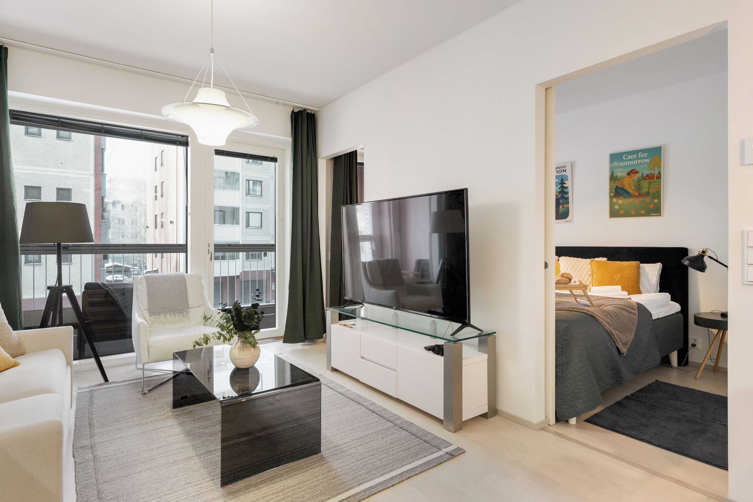 Una habitación de hotel moderna con un televisor grande, un sofá, una mesa de centro de vidrio y una cama con cabecera negra.