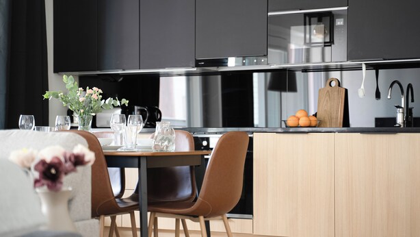 A modern kitchen with dark cabinets, stainless steel appliances, a wooden island, and a dining area with a table and chairs. - Vapari - Tampere Soccer Stadium by Come in! (Tampere)