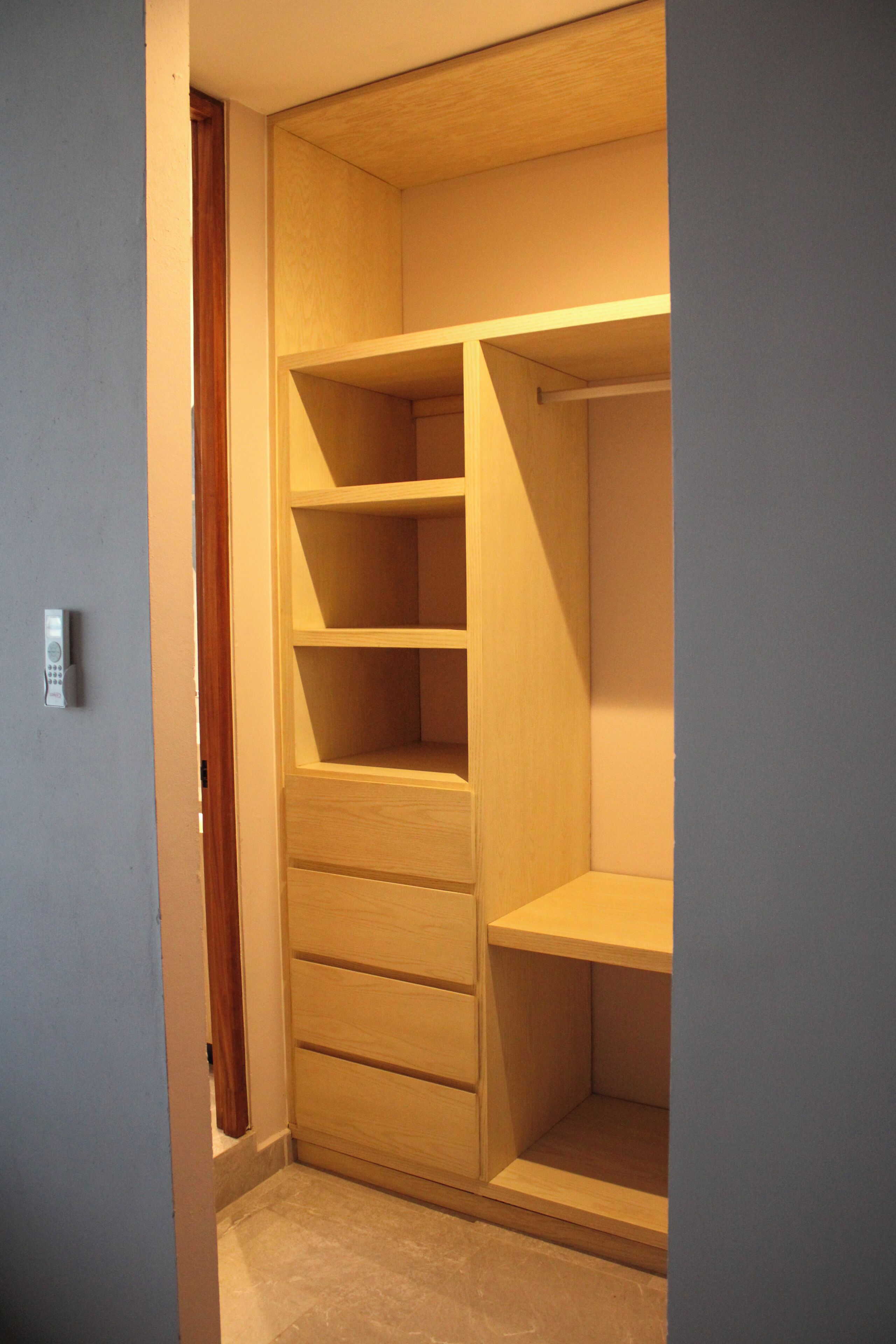 A walk-in closet with multiple shelves and drawers, a wooden door, and a light switch on the wall.