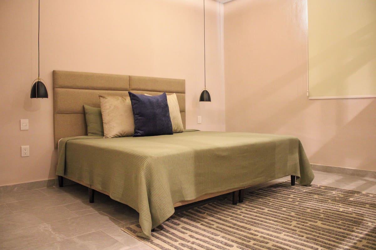 Ein Schlafzimmer mit einem Bett, einem Kopfteil, zwei Nachttischlampen und einem gemusterten Teppich.
