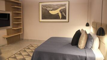 A modern bedroom with a bed, pillows, a wall-mounted TV, a framed artwork, and a patterned rug.