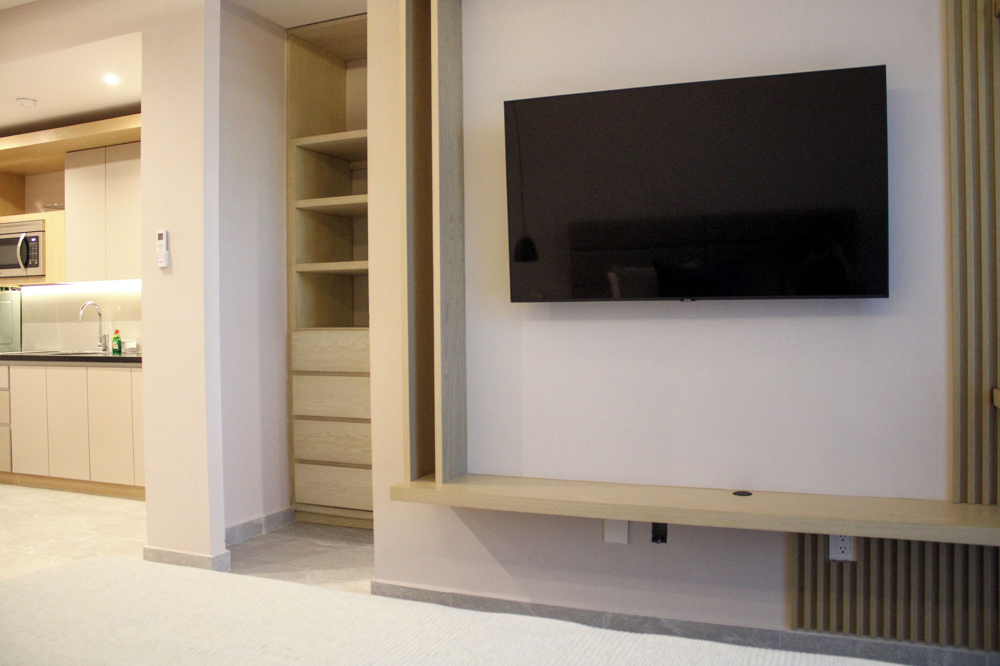 Een modern interieur met een flatscreen televisie aan de wand, een keuken met een magnetron en een trap naar een hoger gelegen niveau.