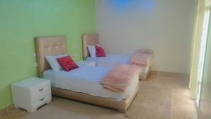 A bedroom with two beds, each with a headboard, a nightstand, and a drawer unit.