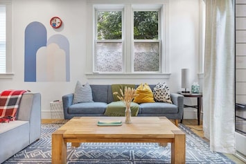 The living room is bright and spacious, featuring comfortable seating perfect for relaxing or entertaining. Large windows flood the space with natural light, creating a welcoming atmosphere for your stay. 🛋️☀️