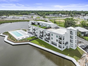 Ein modernes Gebäude mit Schwimmbad, mehreren Balkonen und einem Parkplatz.