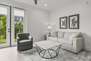 A modern living room with a grey sofa, a grey armchair, and a marble coffee table. There are two framed abstract paintings on the wall. - Brand New 1 Bedroom Condo-Luxurious Waterfront Pool-Sleeps 4 (Gulfport)