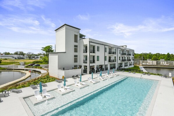 A modern building with a swimming pool, lounge chairs, and a small water feature.