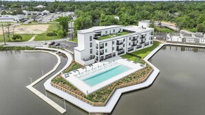 A modern hotel with a central swimming pool, surrounded by a dock and landscaped areas. - Brand New 2 Bedroom Condo-Luxurious Waterfront Pool-Sleeps 4 (Gulfport)